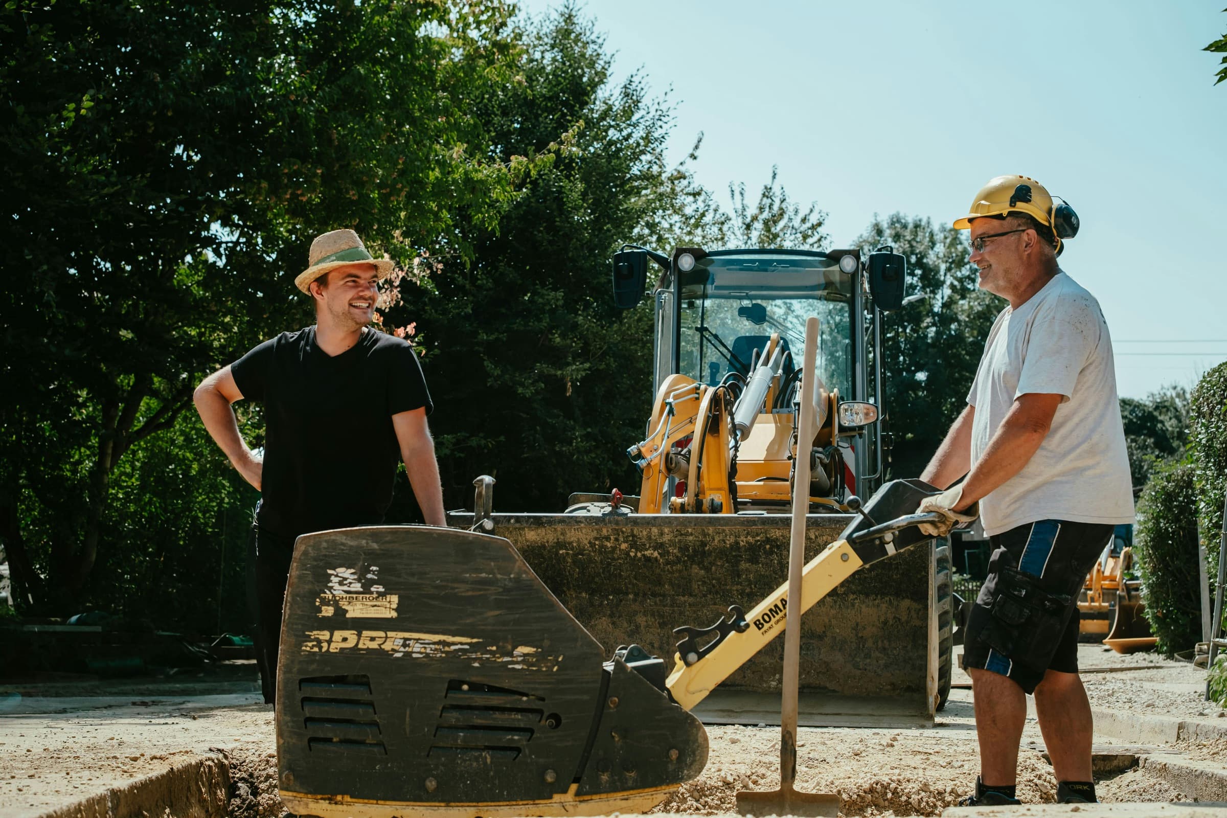 Zwei Mitarbeiter von Seel Bau sprechen auf einer sonnigen Baustelle miteinander